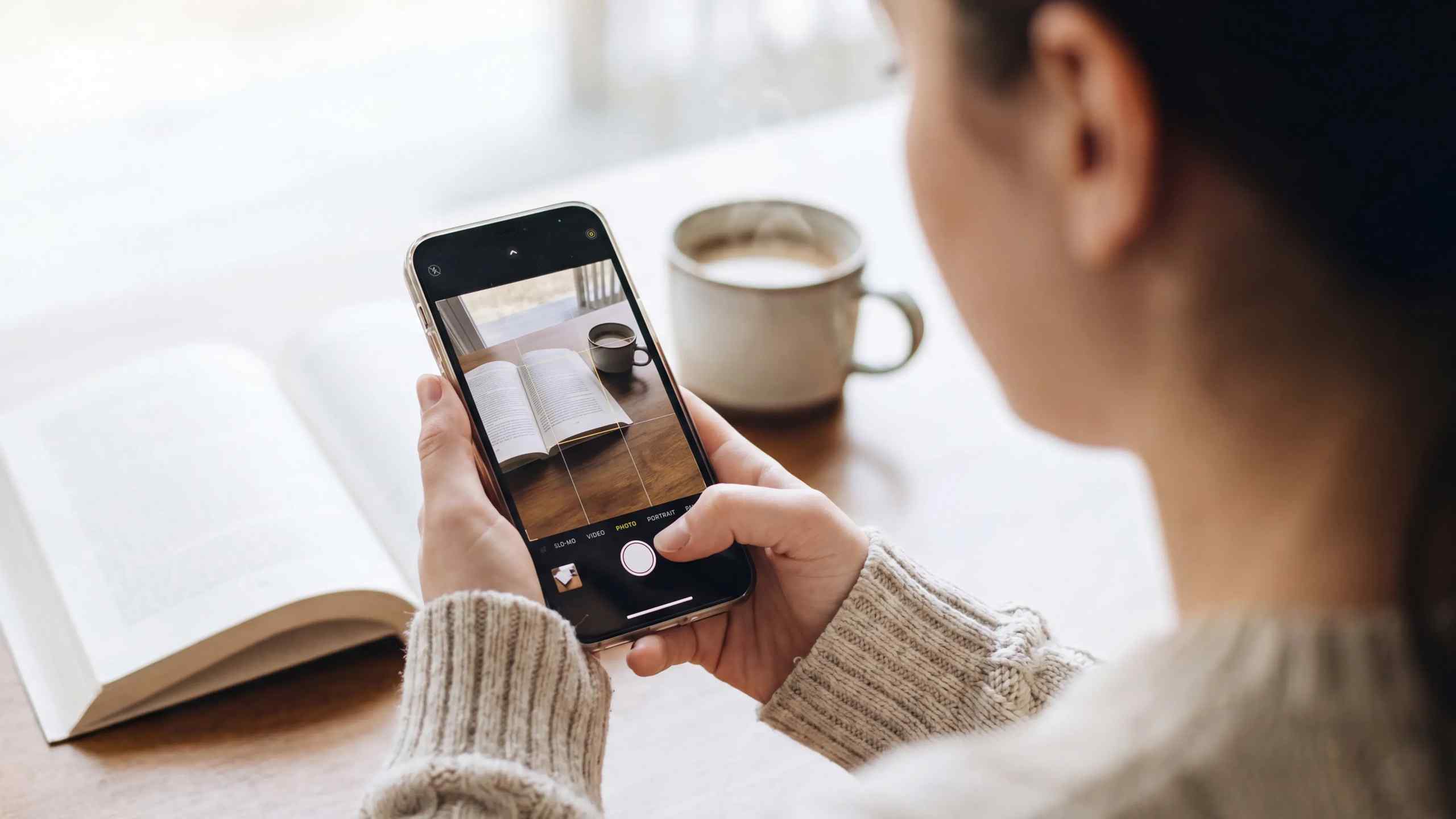 A woman taking a photo on her smart phone of a book and coffee